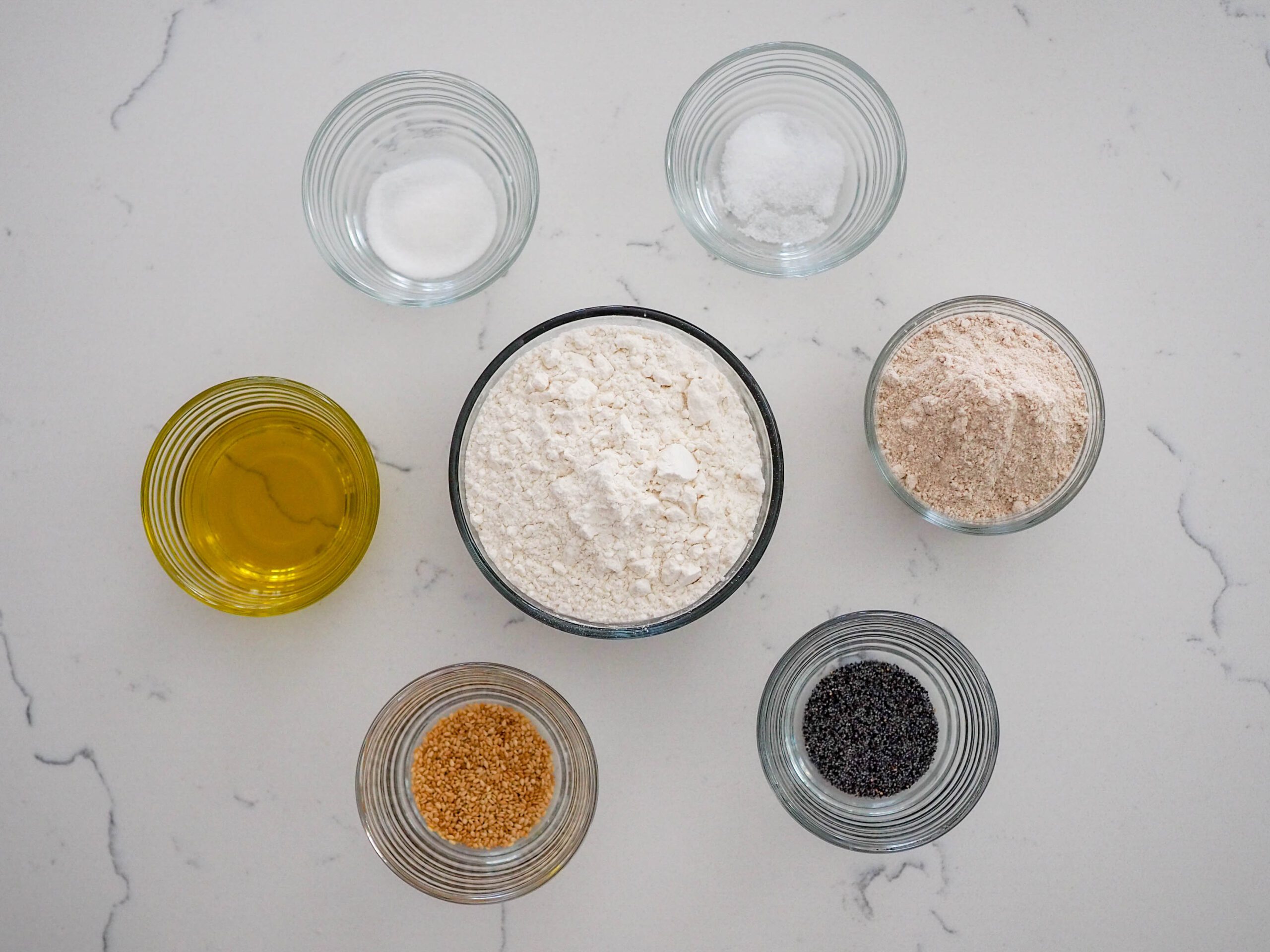 Ingredients for sesame and poppy seed crackers: olive oil, sugar, salt, whole wheat flour, poppy seeds, sesame seeds, and flour.