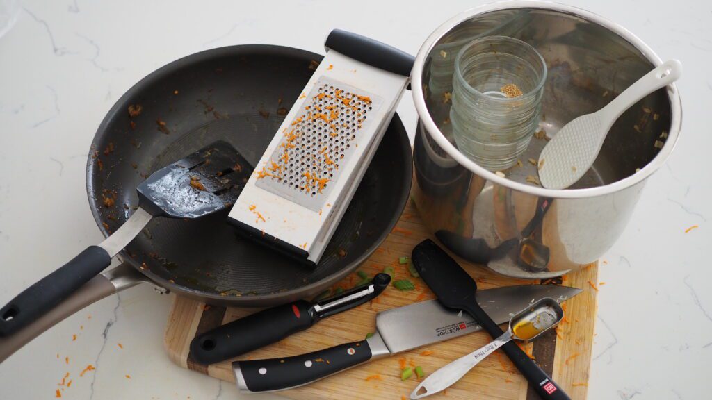 A fry pan, Instant Pot pot, and various kitchen utensils lay on a cutting board