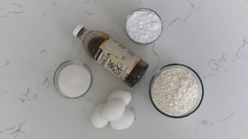 Sugar, vanilla, powdered sugar, flour, and eggs arranged on a quartz counter.