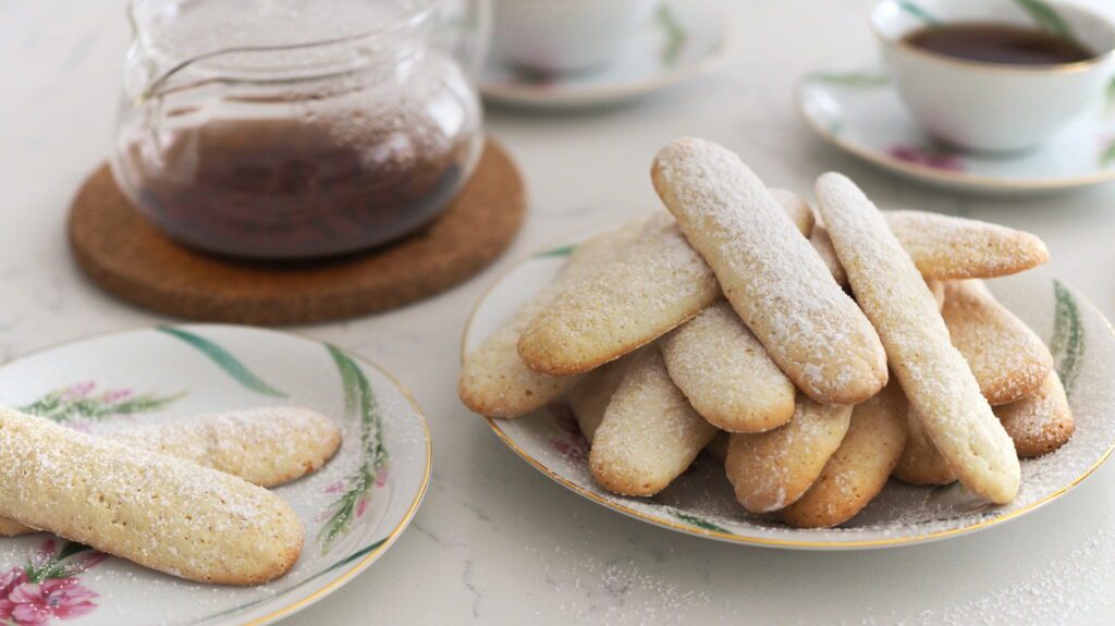 A pile of ladyfingers on a platter with tea.