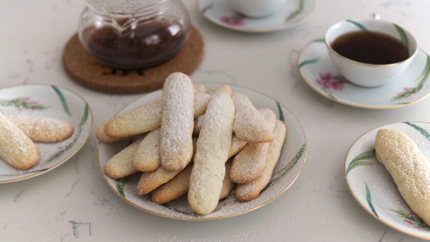 A plate of ladyfingers amid tea saucers and cups of tea.