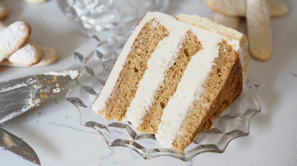A slice of three-layer tiramisu cake is on its side on a crystal plate.