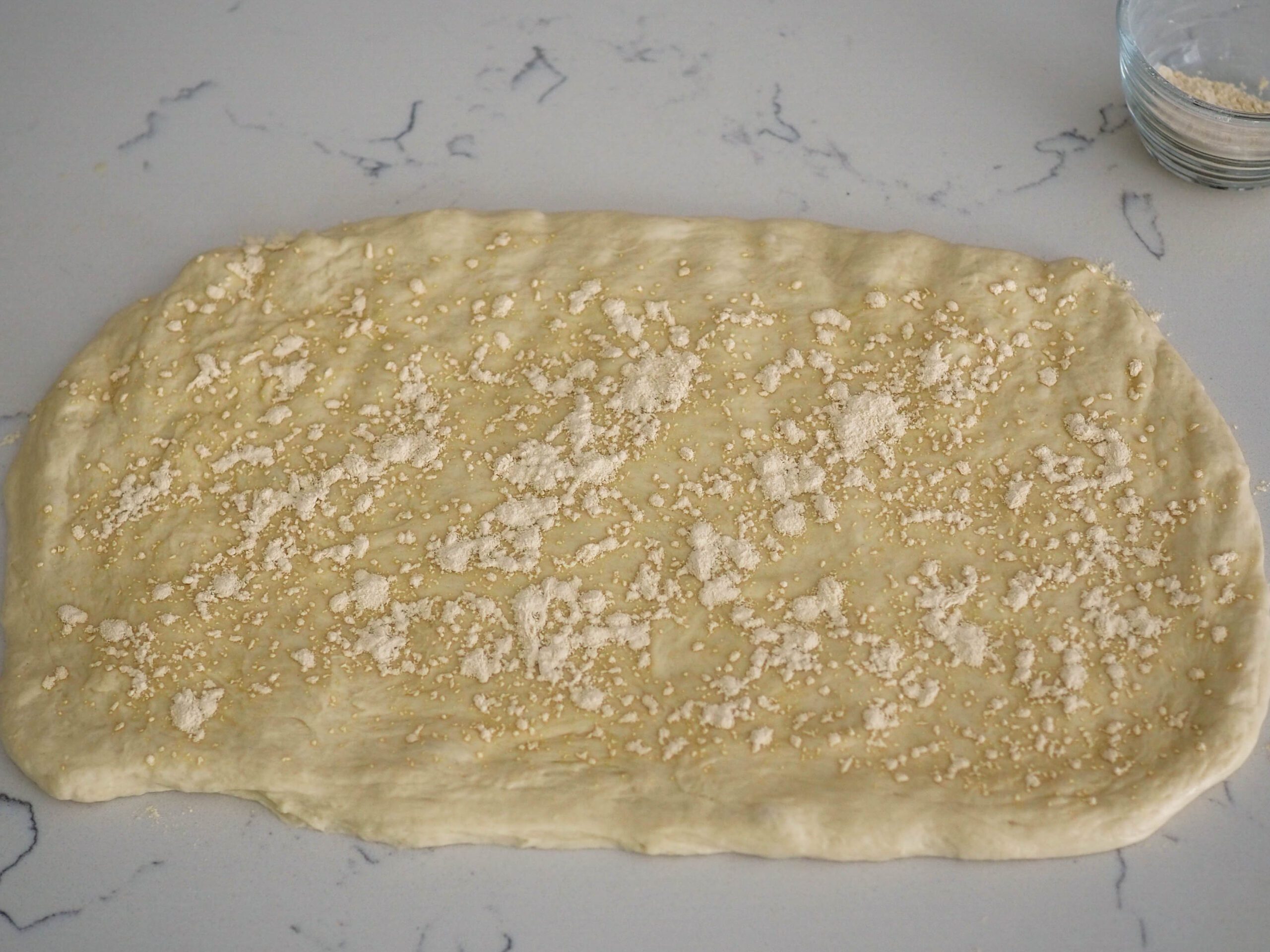 A rectangle of French bread dough with garlic powder sprinkled unevenly on top of it.