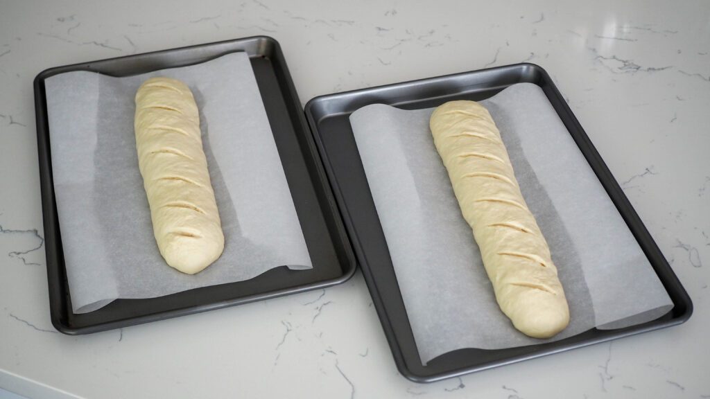 Two unbaked loaves of garlic bread, slit across the top diagonally.