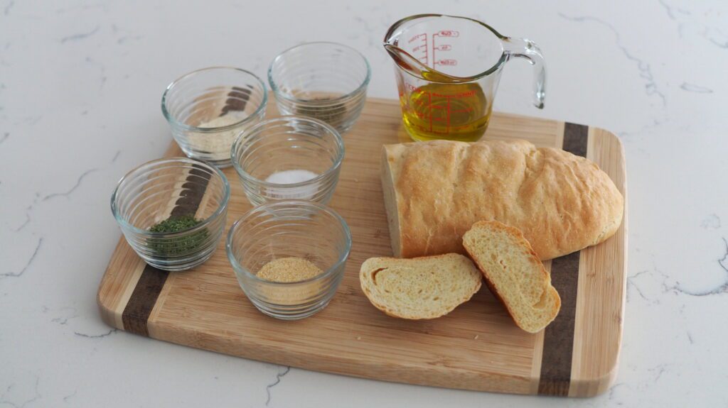 Half of a loaf of garlic French bread, oil, and seasonings on a wooden cutting board.