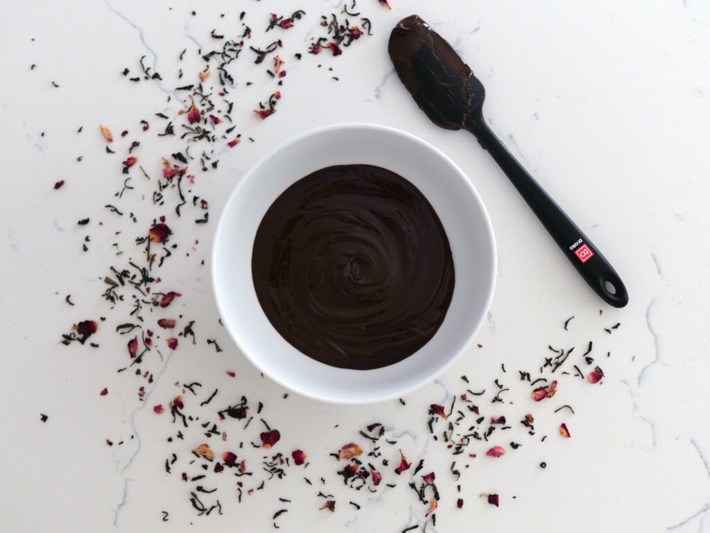 A white bowl with rosy earl grey ganache in the center, ringed by rosy earl grey tea and a black spatula.