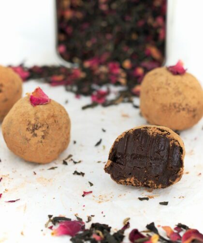 A half-eaten rosy earl grey truffle surrounded by five other truffles and tea.