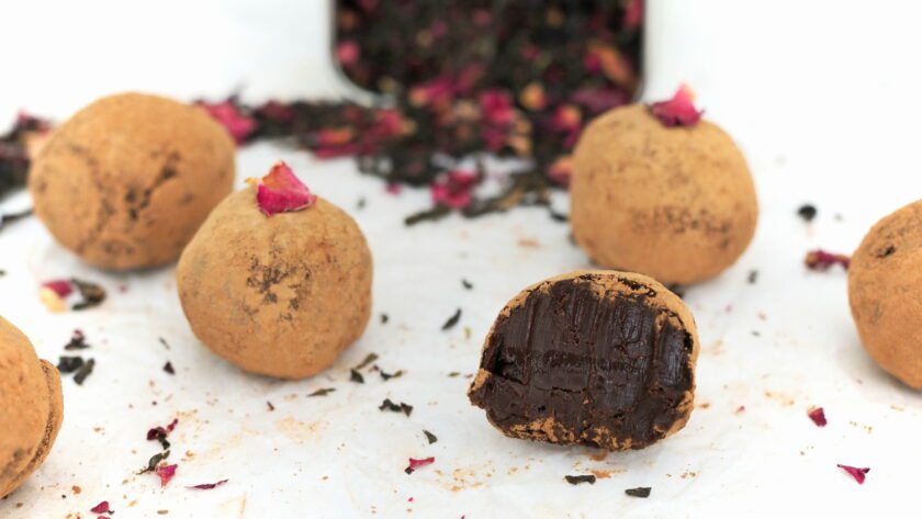 A half-eaten rosy earl grey truffle surrounded by five other truffles and tea.