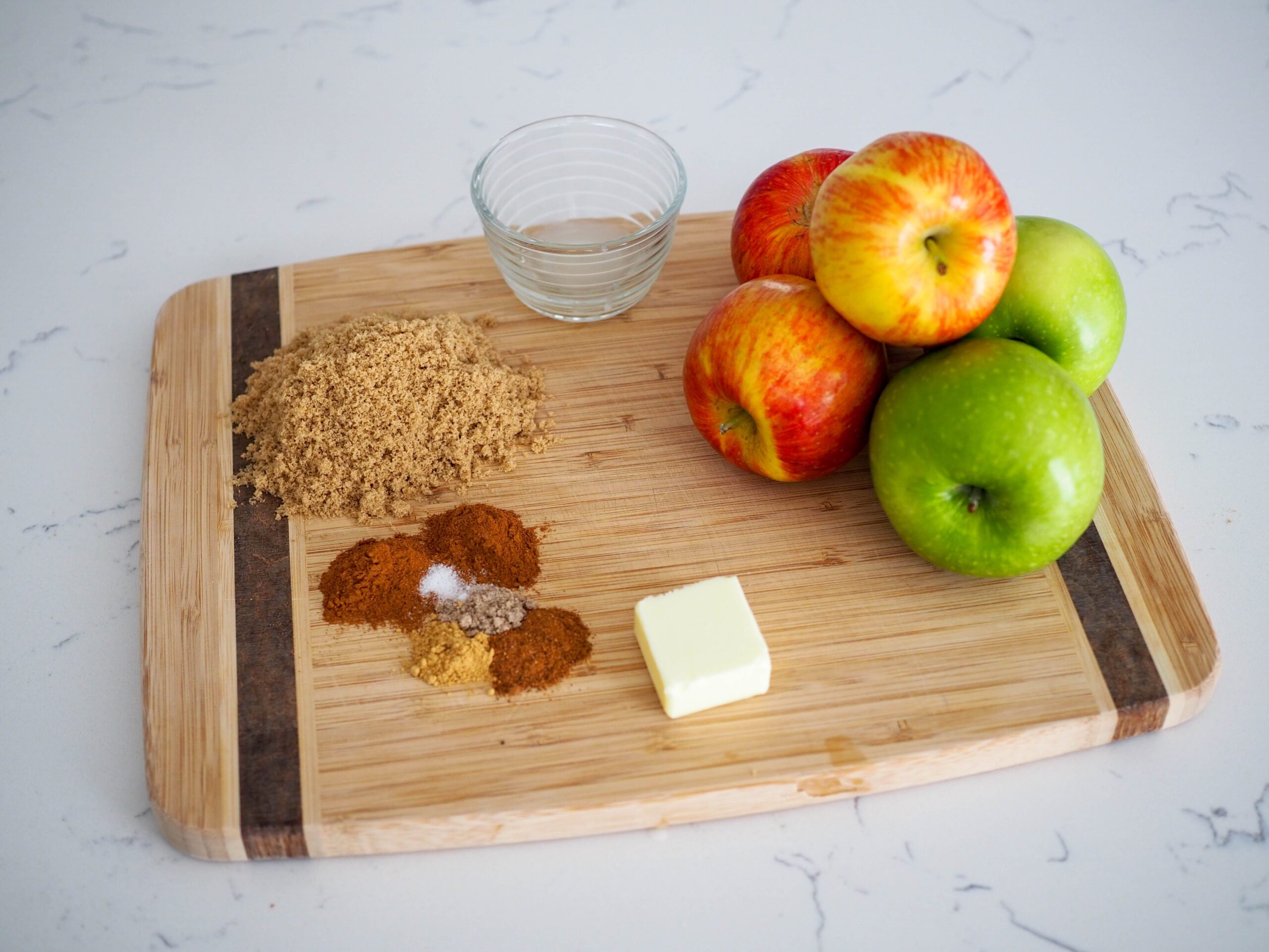 Spices, brown sugar, lemon juice, apples, and butter on a wooden cutting board