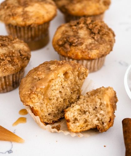 A caramel chai muffin cut in half, next to four other muffins, caramel sauce, star anise pods, cinnamon sticks, and a cup of chai tea.