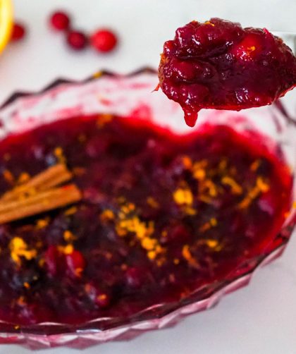 A spoon takes a heaping serving of cranberry sauce, with two orange halves and cranberries surrounding it.