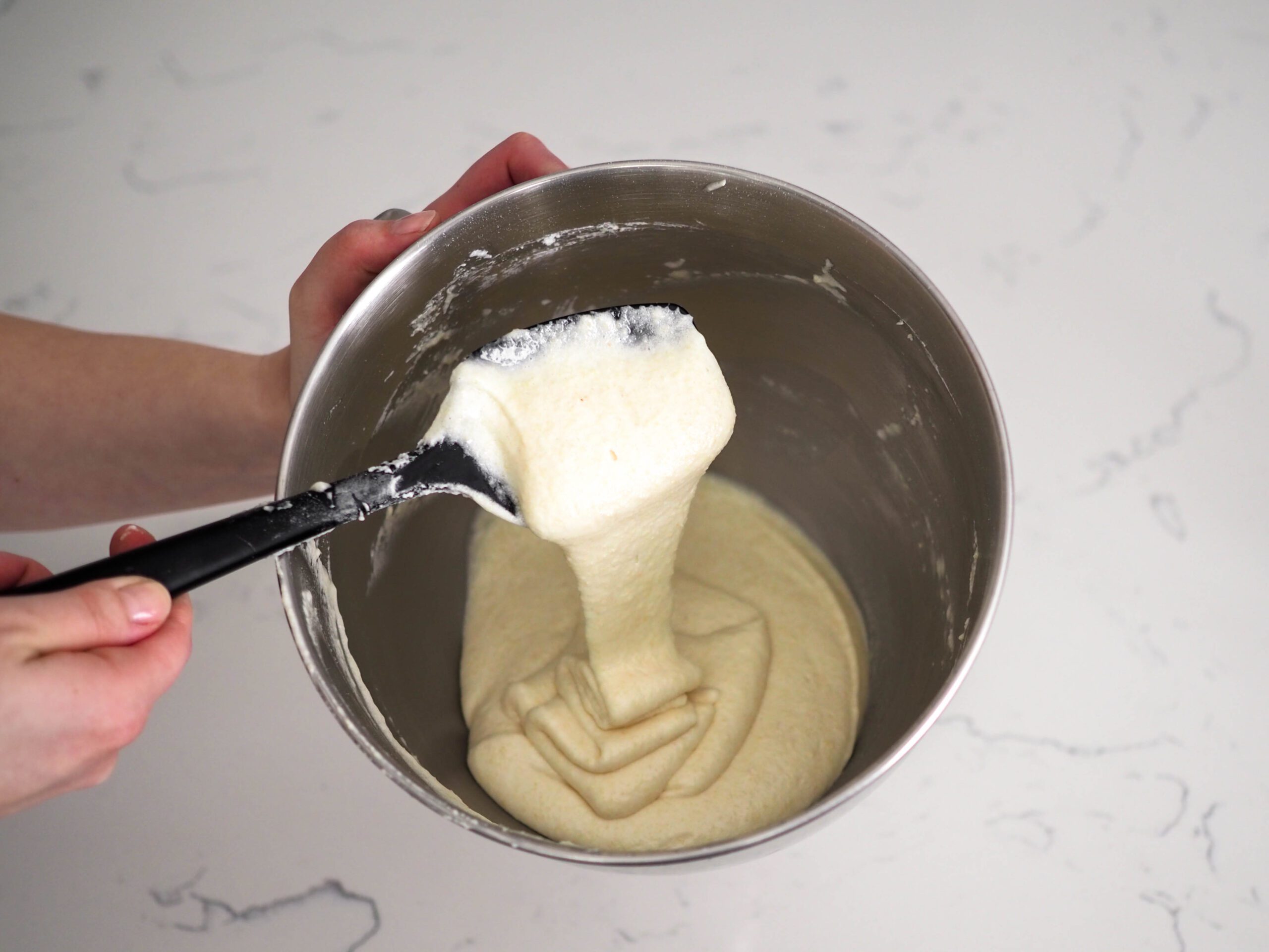 The macaron batter flows off the spatula in one long ribbon that stacks on top of itself in the bowl.
