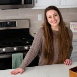 Alyssa stands in her kitchen, smiling, with a hand on her quartz countertop.