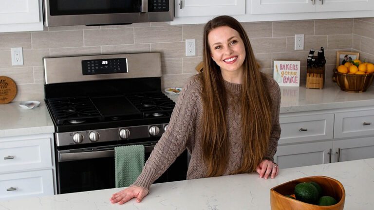 Alyssa stands in her kitchen, smiling, with a hand on her quartz countertop.