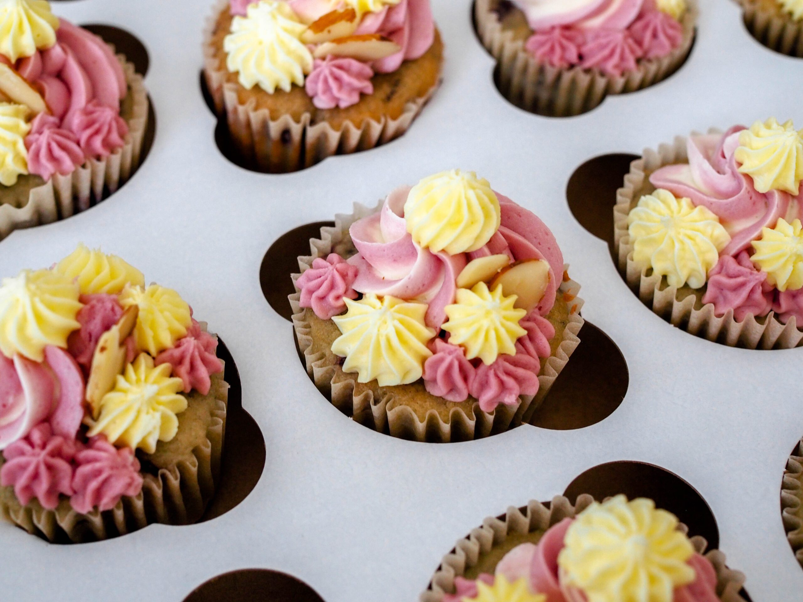 A cherry almond cupcake, decorated with yellow and pink frosting and topped with two almonds.