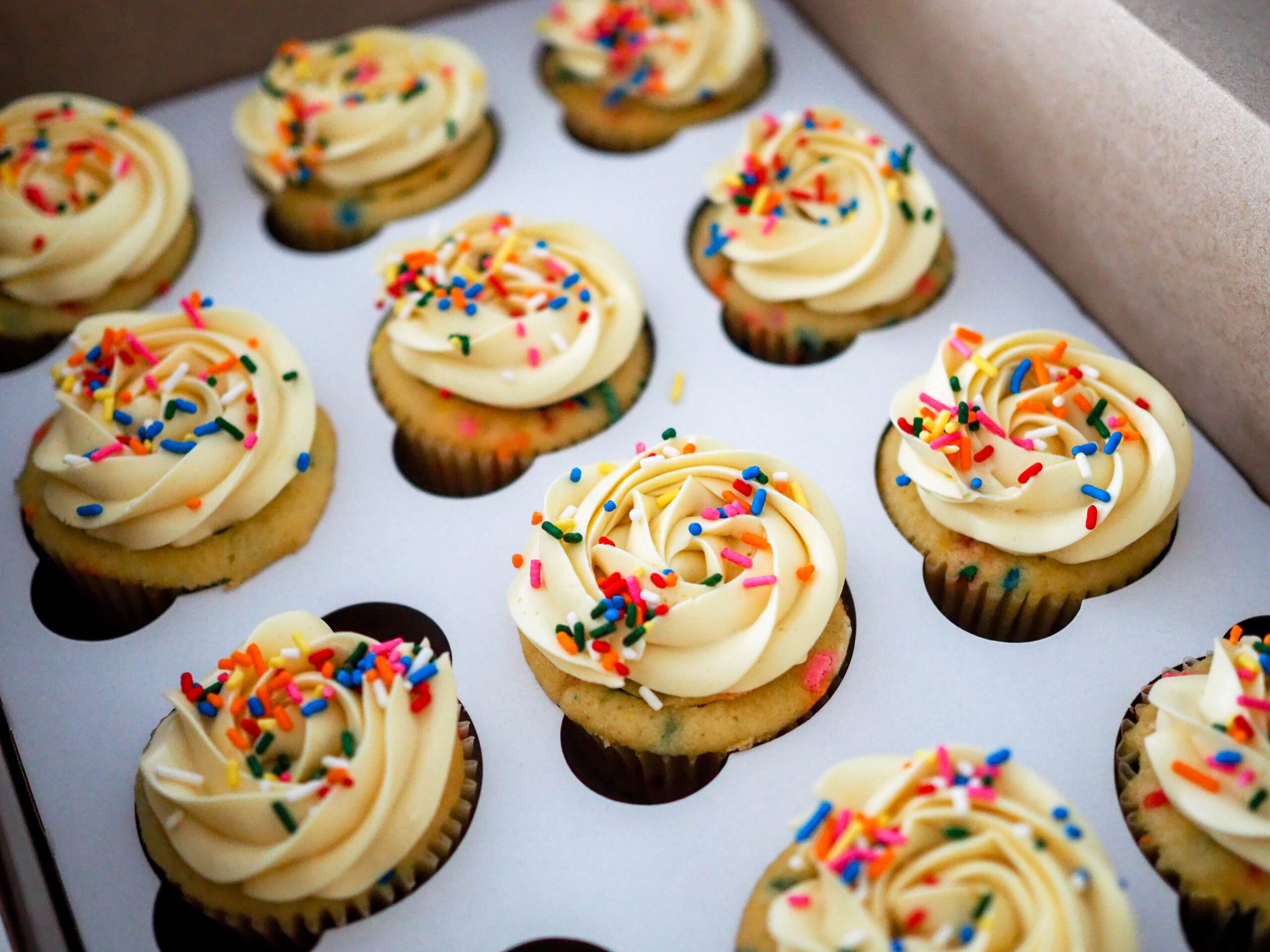 Funfetti cupcakes in a box, decorated with lots of rainbow sprinkles.