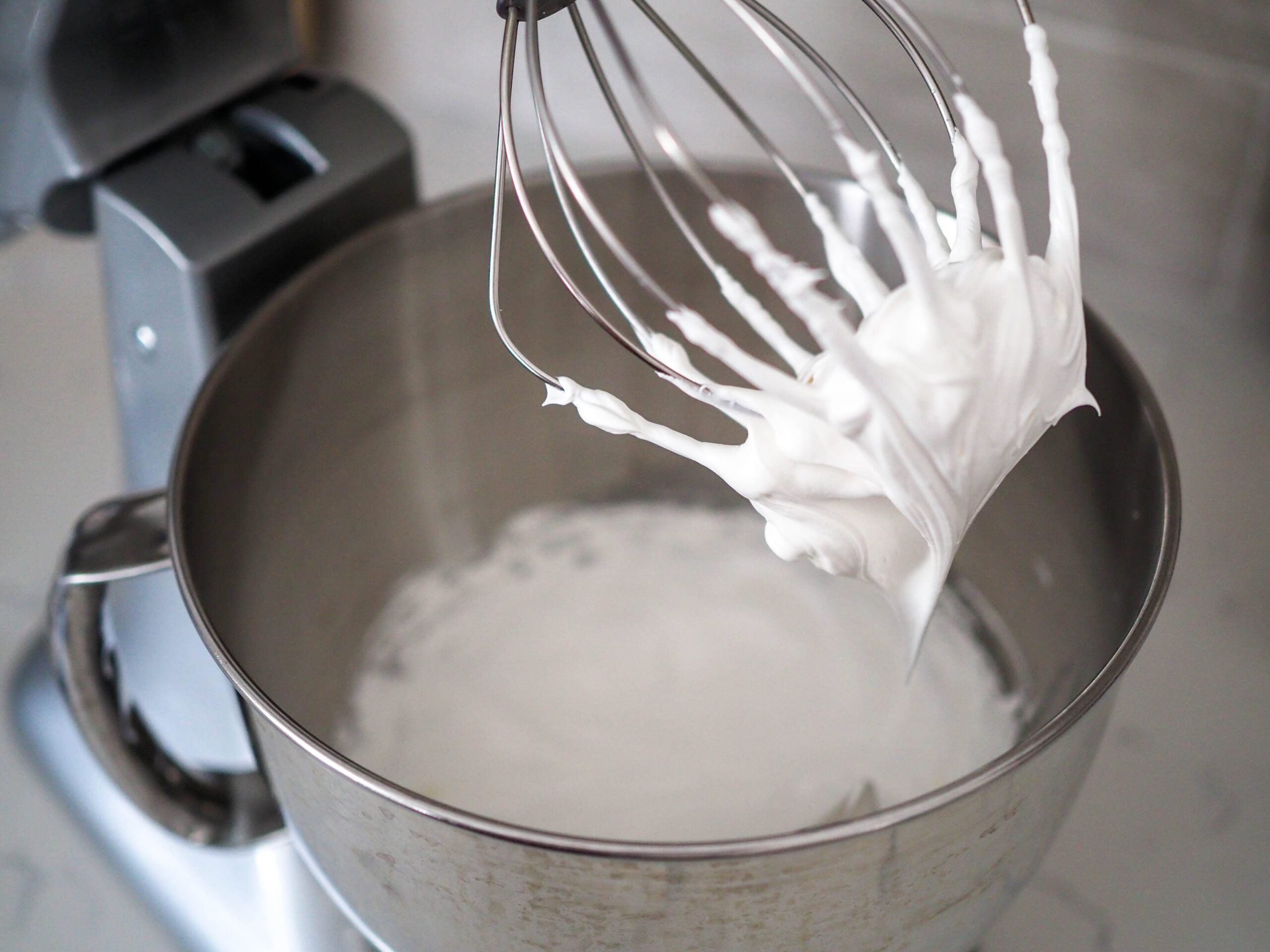 Swiss meringue clumped around the whisk attachment of a stand mixer.