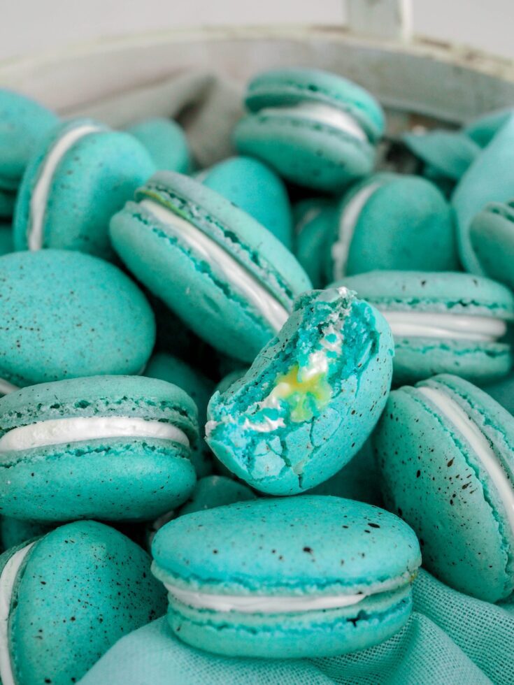 A half-eaten blue speckled macaron has a white meringue filling with a lemon curd center spilling out.