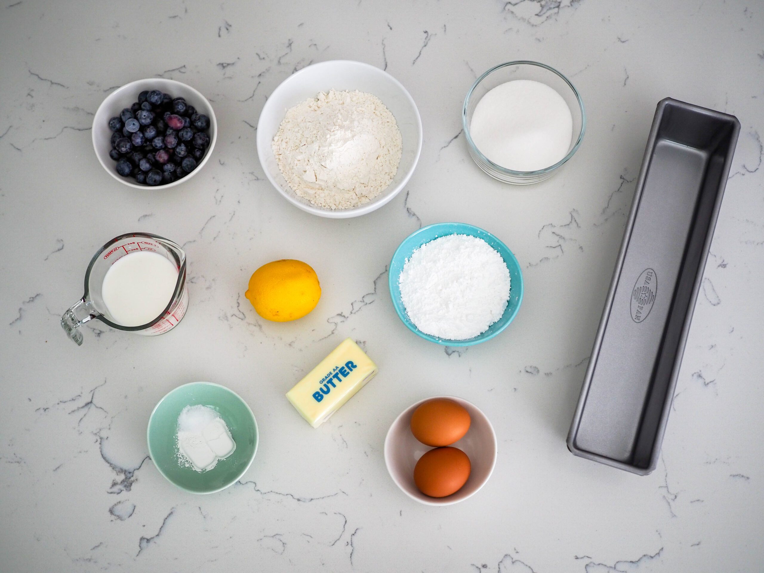 A collection of ingredients arranged on a quartz countertop, with a cocktail loaf pan on the right.