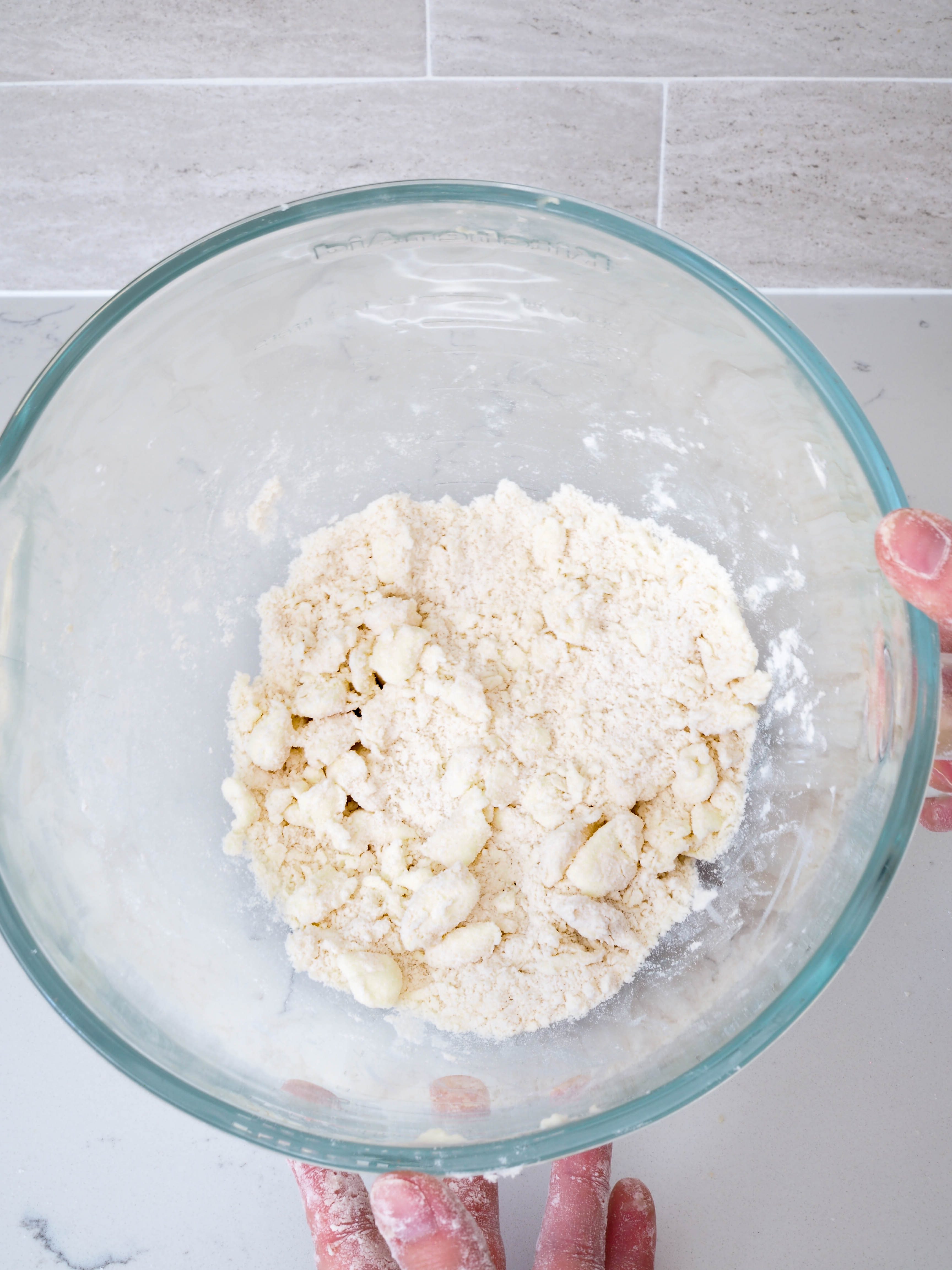 The inside of a glass mixing bowl, with chunks of butter the size of grapes and flour inside of it.