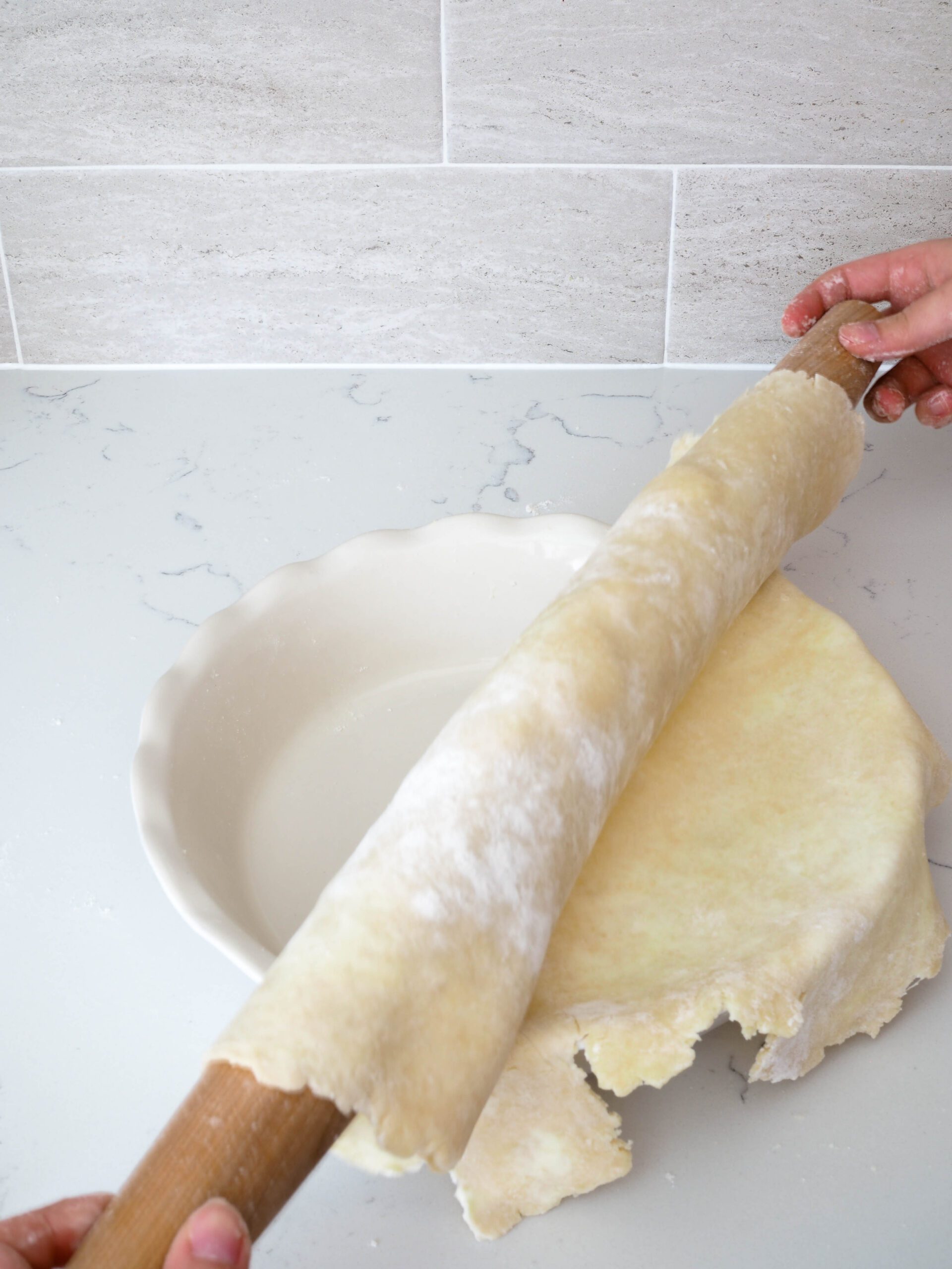 A pie crust is being unrolled off of a rolling pin and into a pie pan.