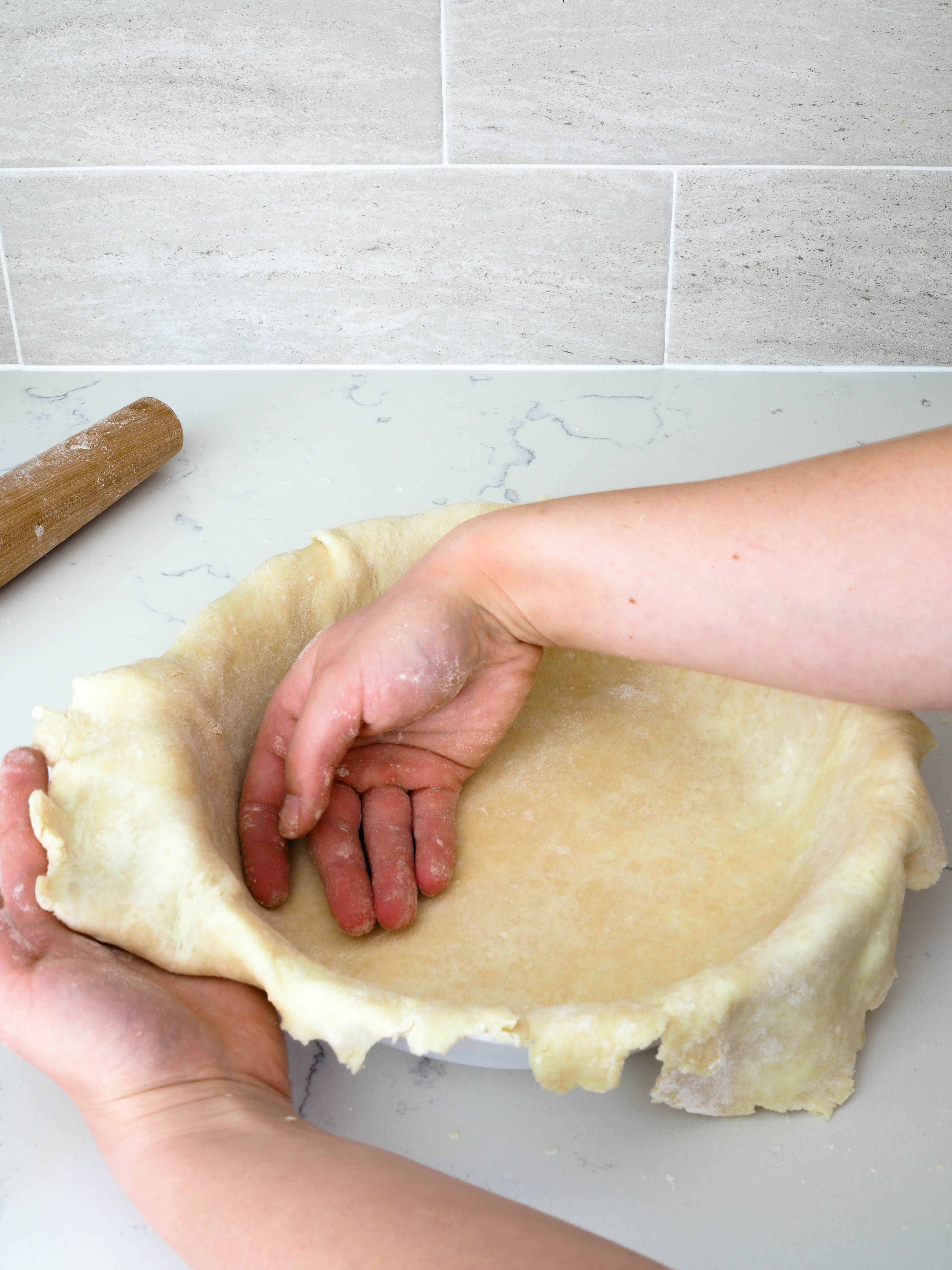 Two hands help gently guide the pie crust into its pan.