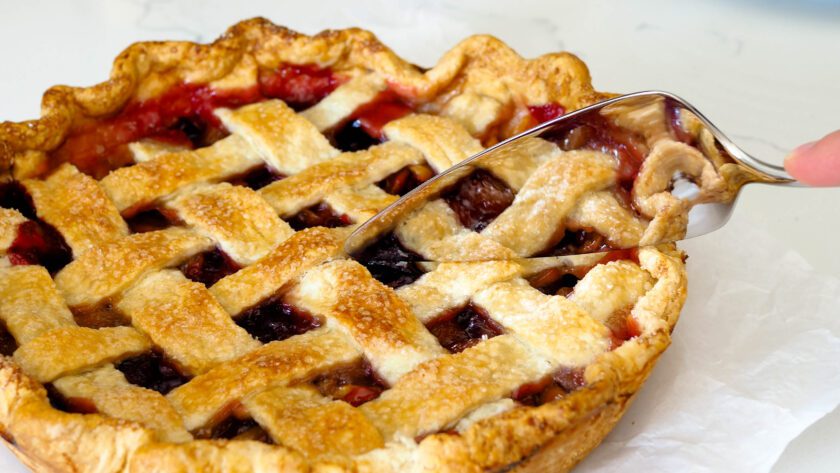 A closeup of a whole cherry pie with a silver server making the first cut into the pie.