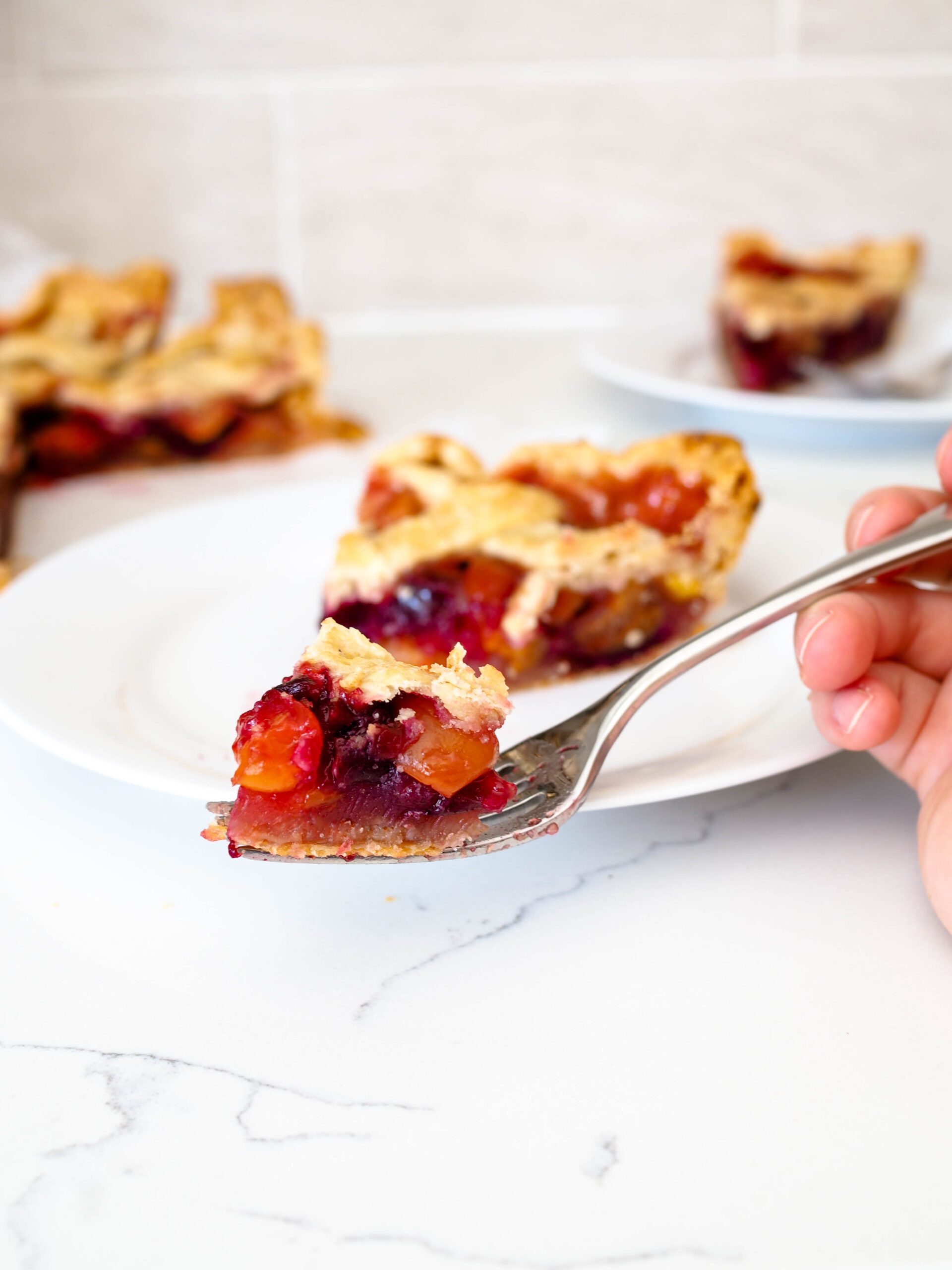 A closeup of a bite of cherry pie on a fork in front of a few slices of pie.