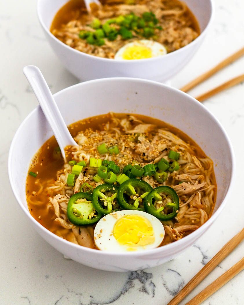 Two bowls of chicken ramen, topped with green onion, jalapenos, and half of a hard-cooked egg.