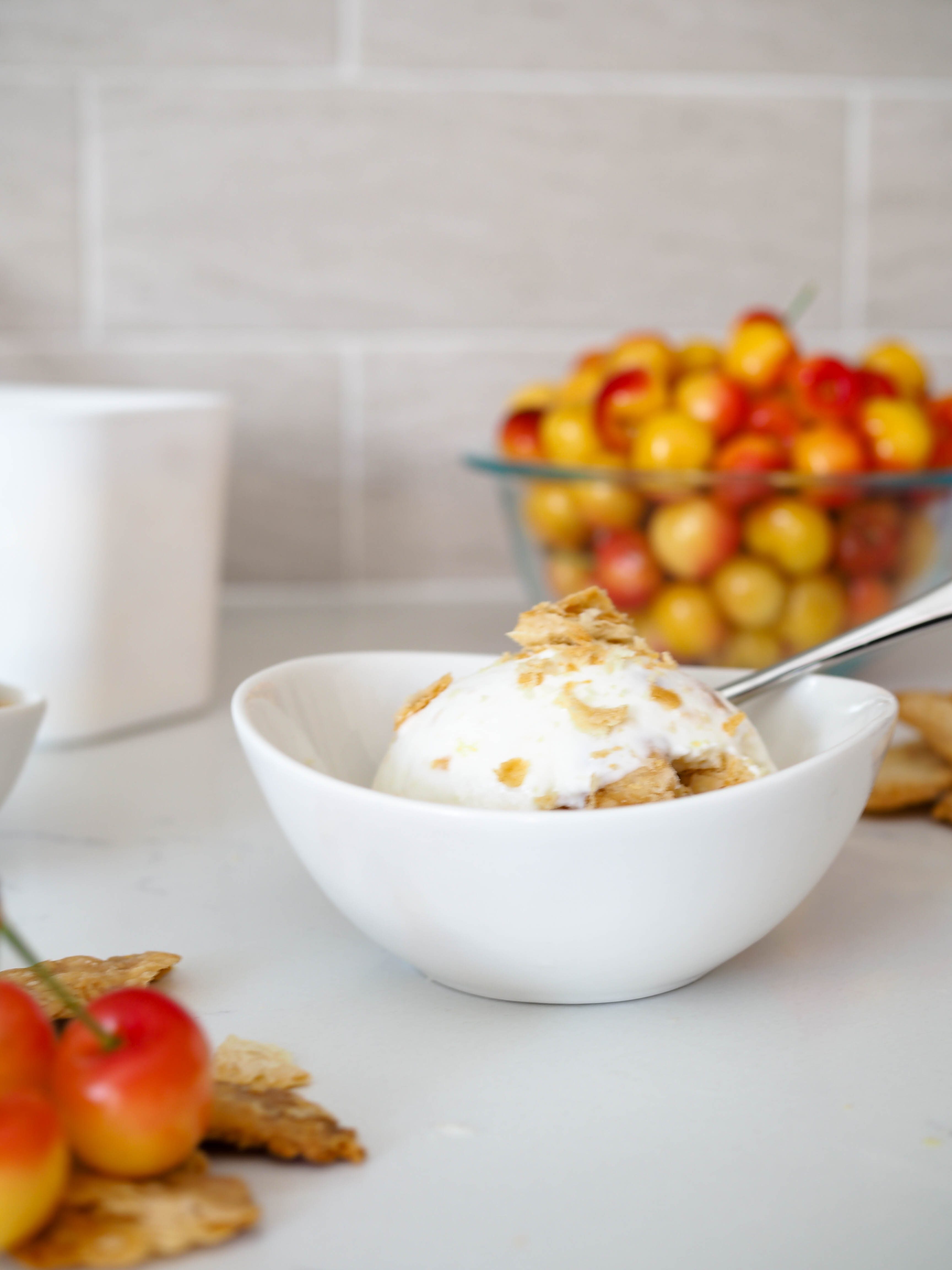 Closeup of a bowl of cherry pie ice cream with Rainier cherries in the background.