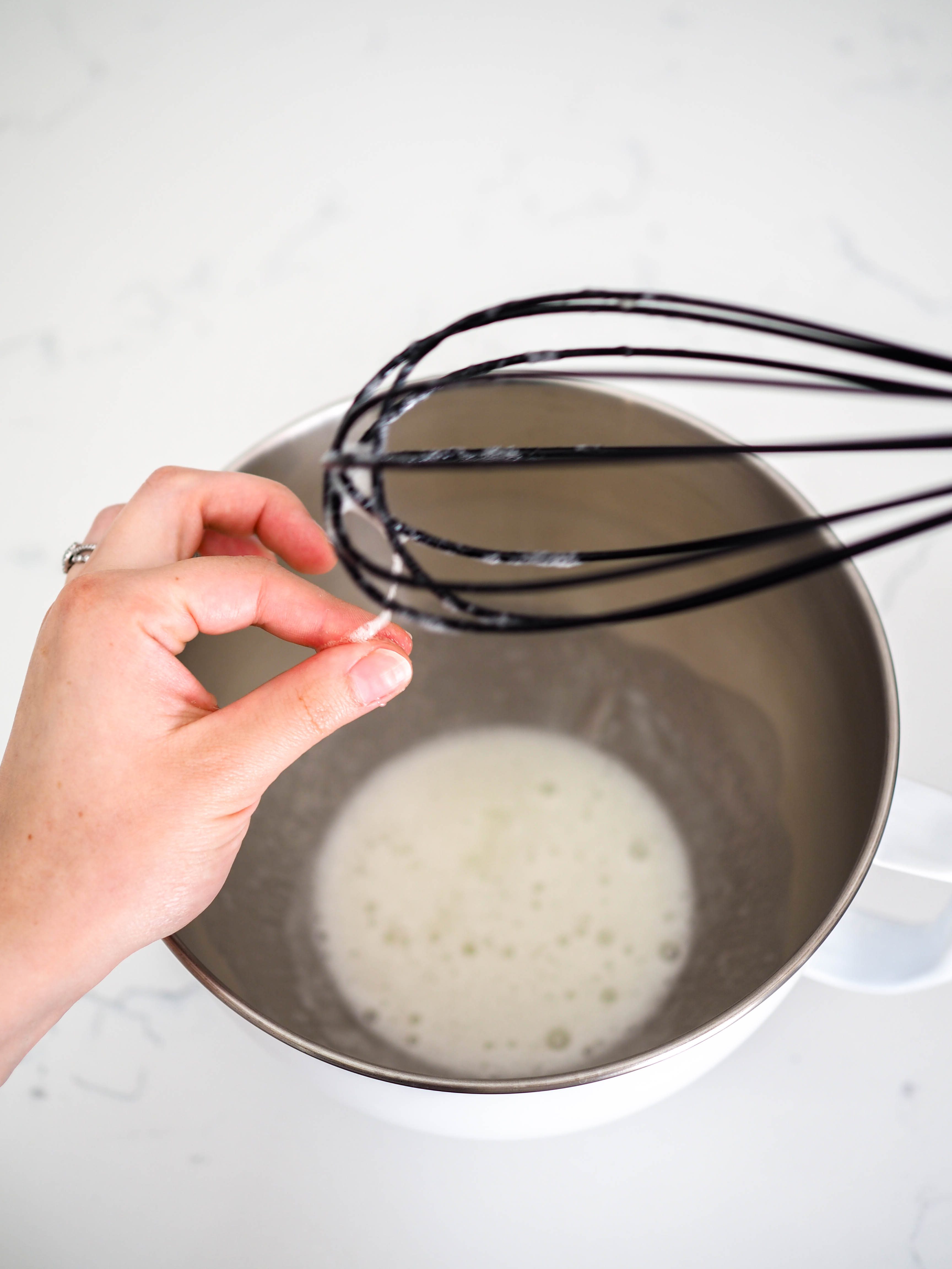 A hand rubs a meringue mixture between a thumb and forefinger.