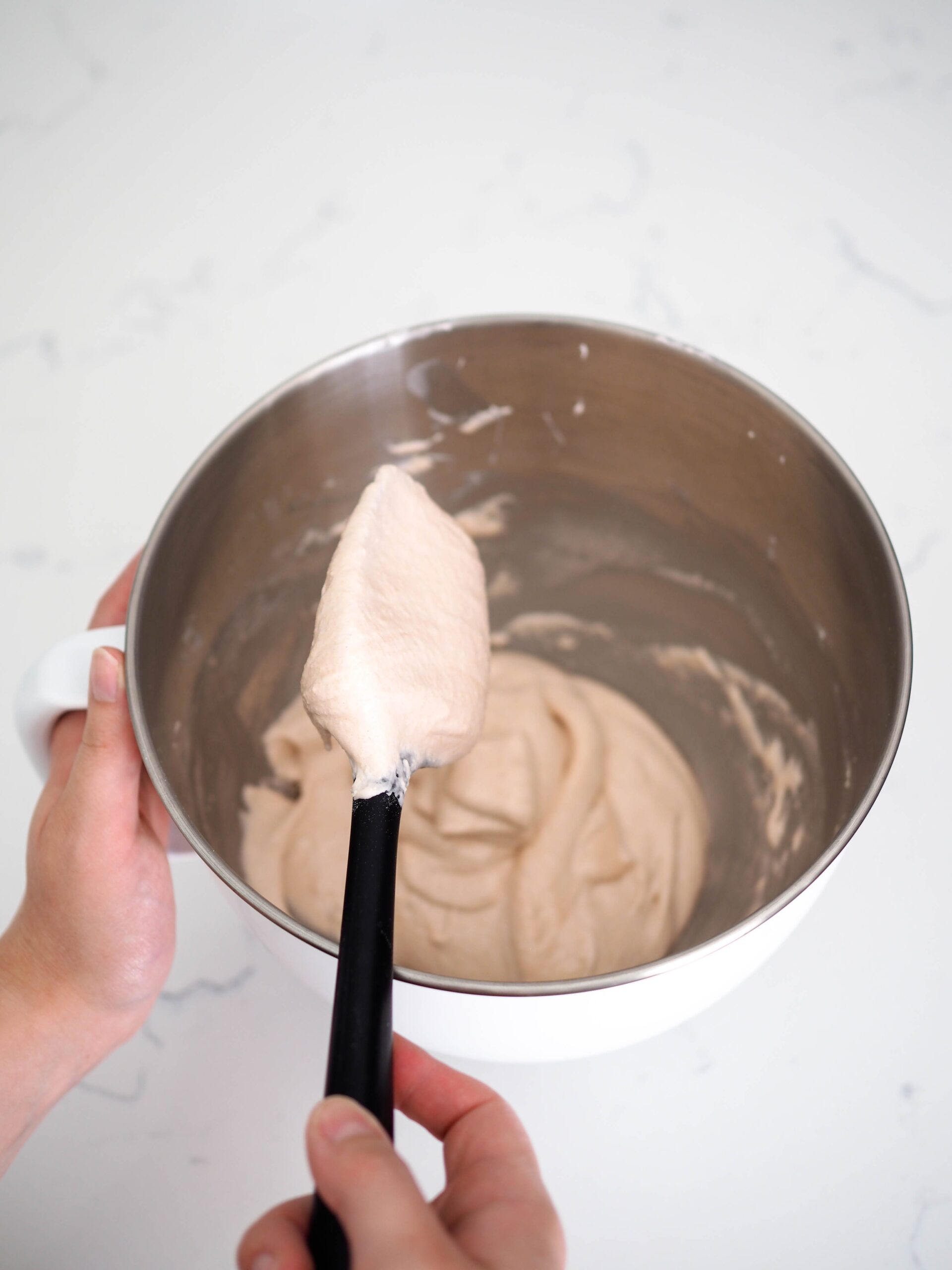 A spatula has macaron batter falling off it in ribbons.