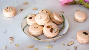 A stack of almond macarons with almond slices on the tops, sitting on a china plate.