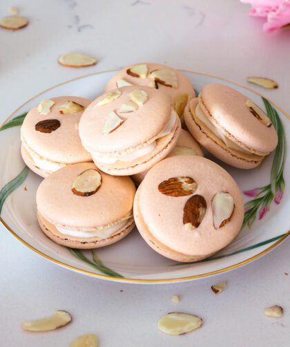 A stack of almond macarons with almond slices on the tops, sitting on a china plate.