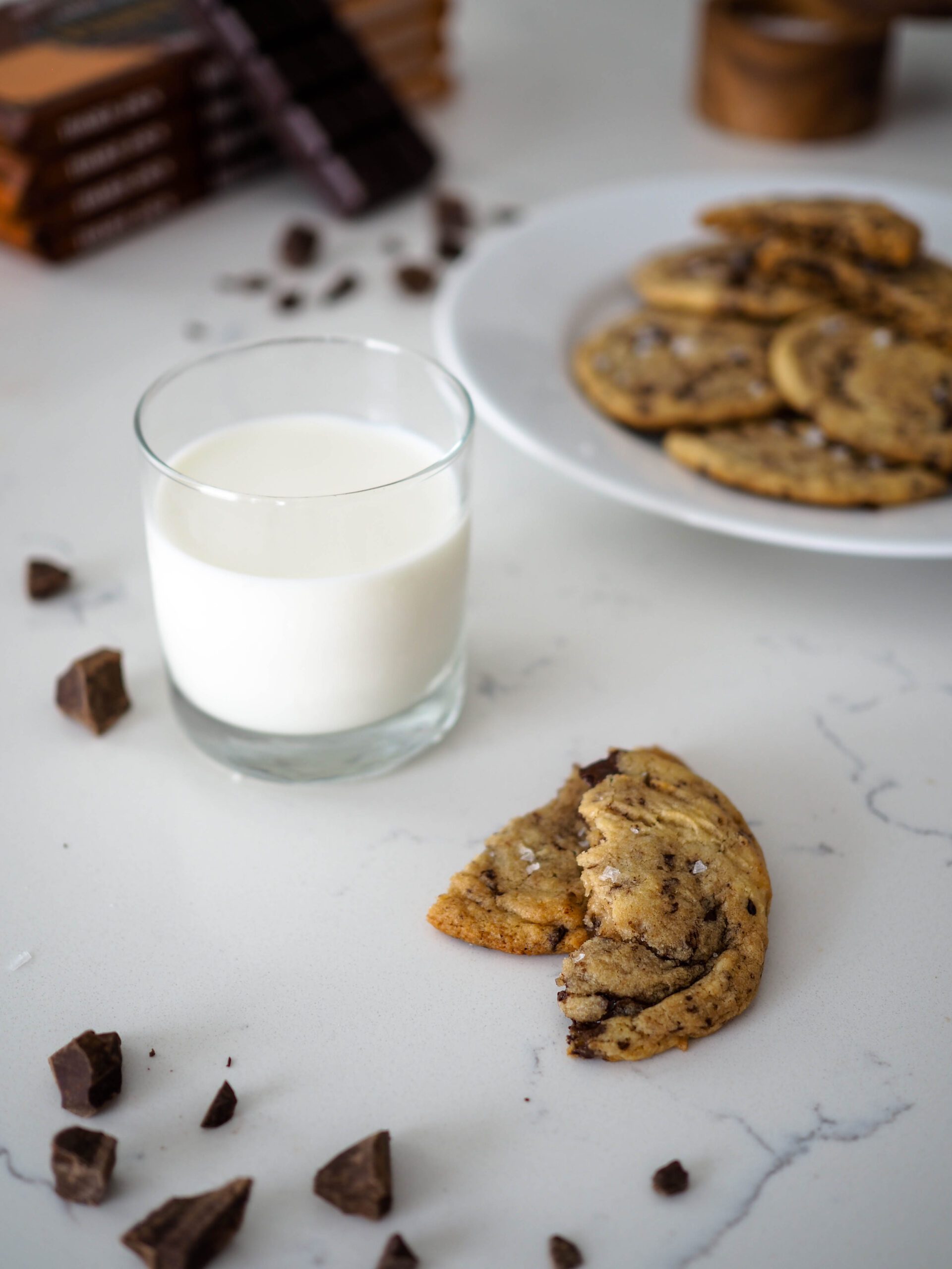 A glass of milk beside two halves of a chocolate chip cookie.