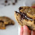 A dark chocolate chunk cookie is broken in half, with melty strings of dark chocolate connecting them.