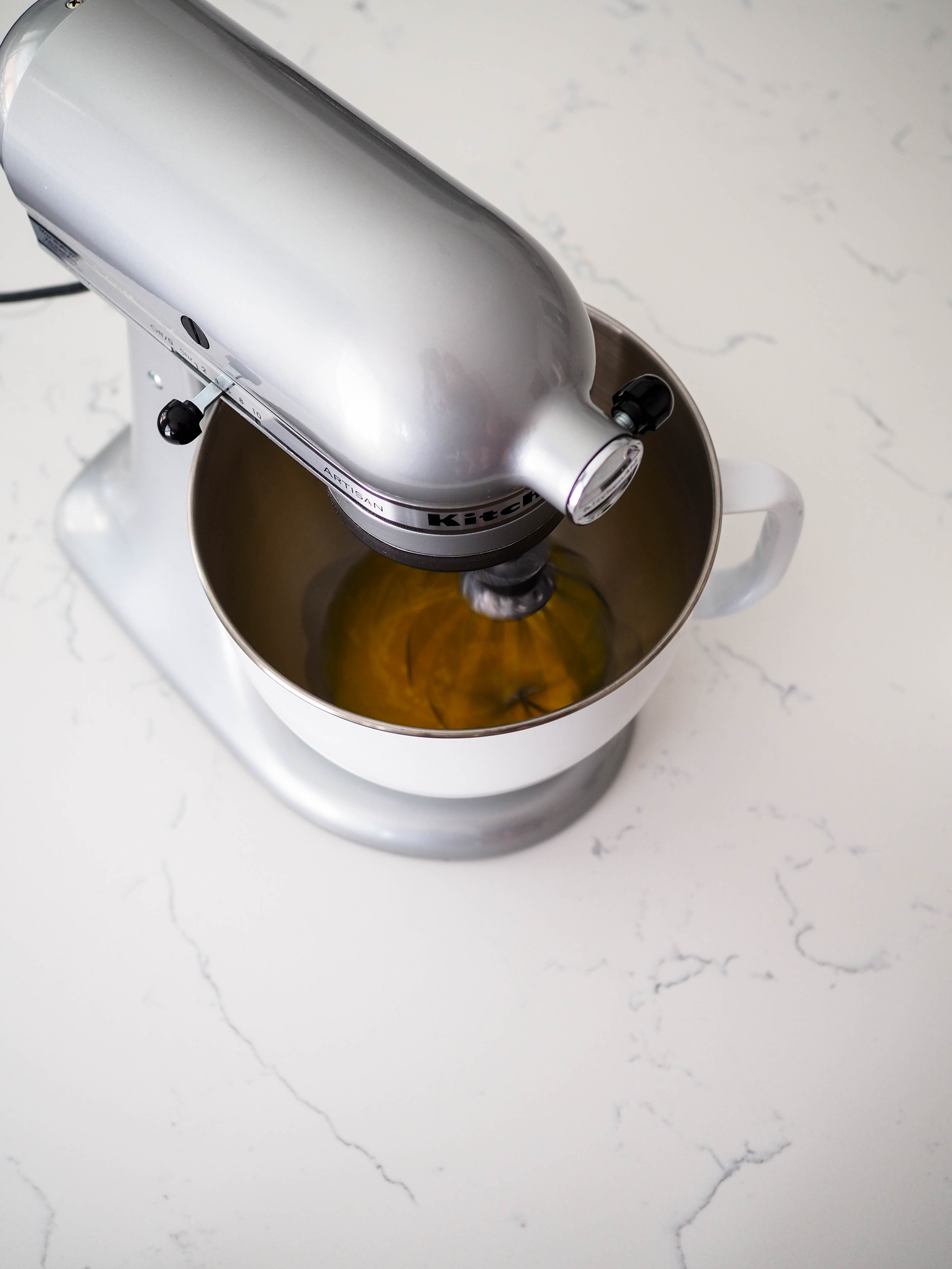 A silver stand mixer is whisking egg yolks.