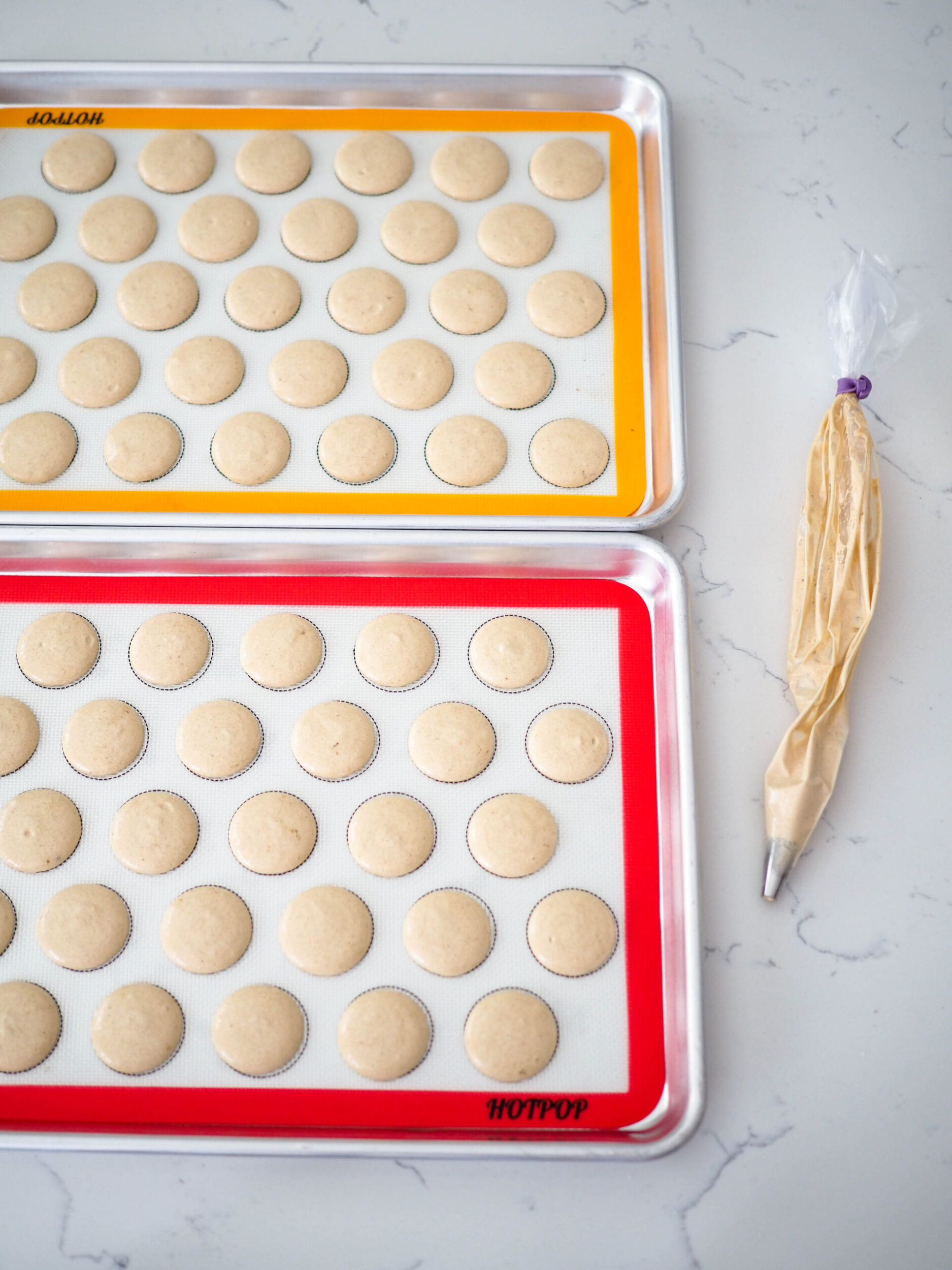 Piped espresso macarons on a marbled quartz background.