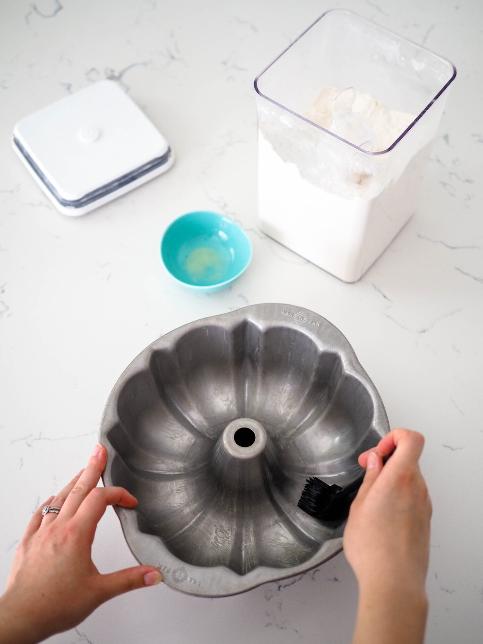 Two hands brush melted butter into a Bundt pan.