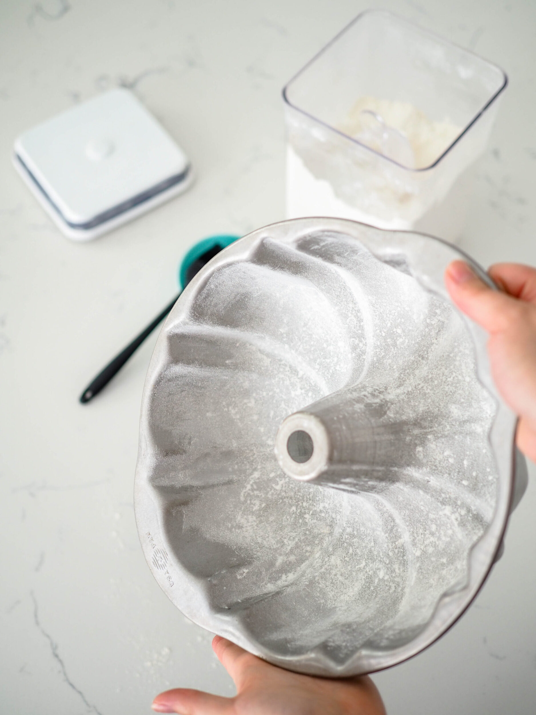 Two hands hold a Bundt pan at an angle, patting flour around inside of it.