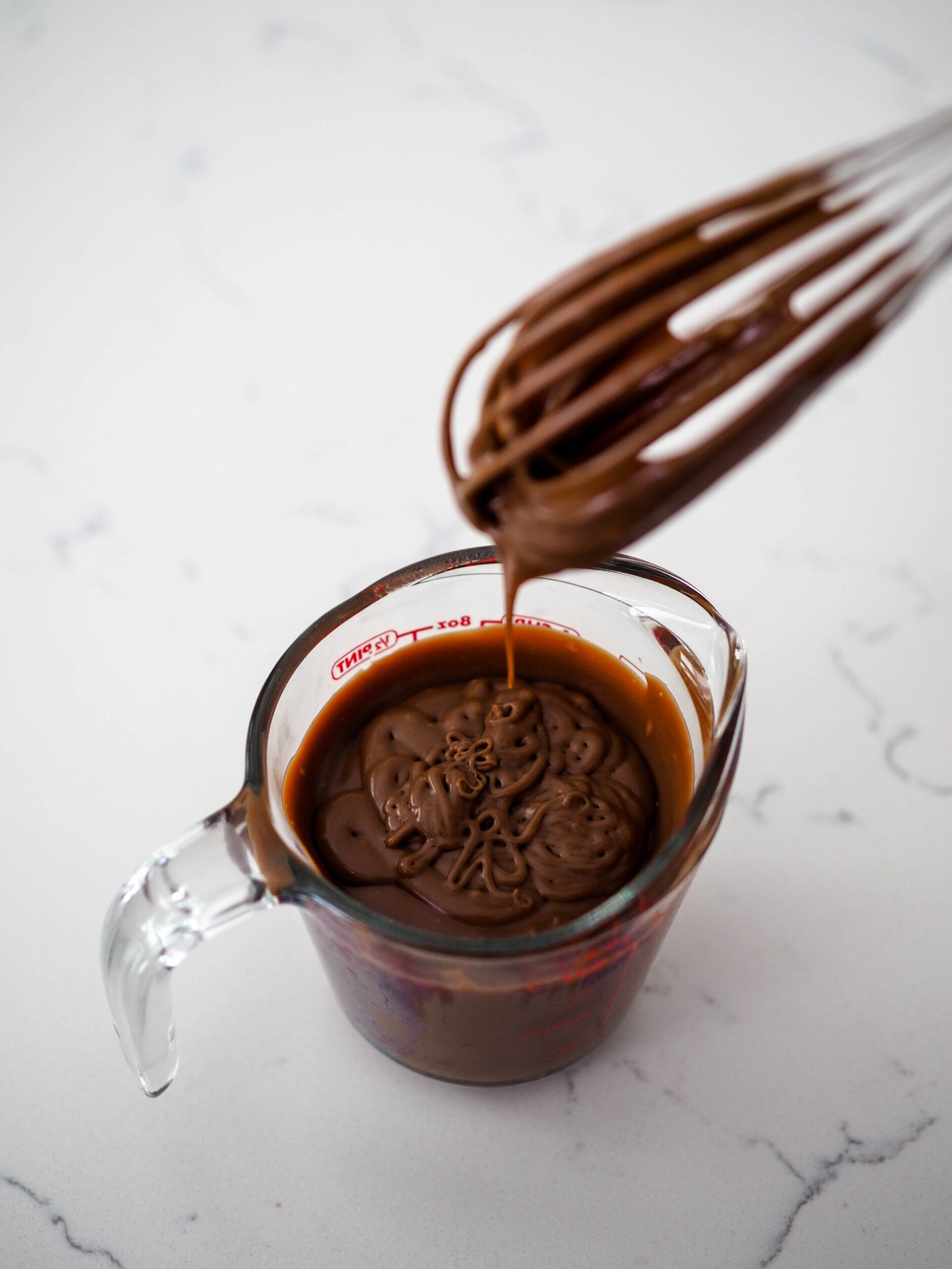A whisk holds up a clump of milk chocolate ganache.