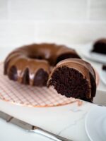 A slice of chocolate Bundt cake is held up near the camera.