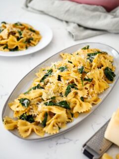 A platter of bowtie pasta with wilted spinach and an orangey-red Cajun sauce.
