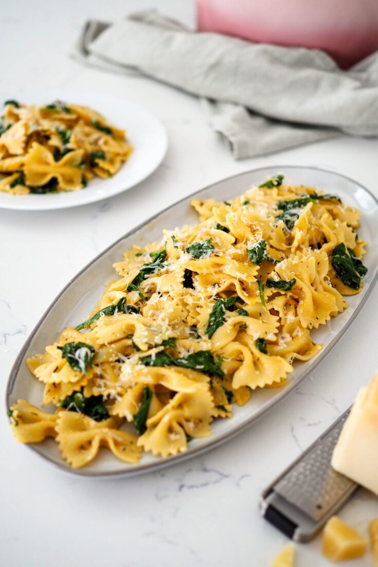 A platter of bowtie pasta with wilted spinach and an orangey-red Cajun sauce.