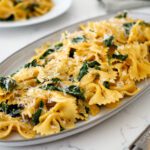 A platter of creamy Cajun spinach pasta with a block of Parmesan cheese nearby.