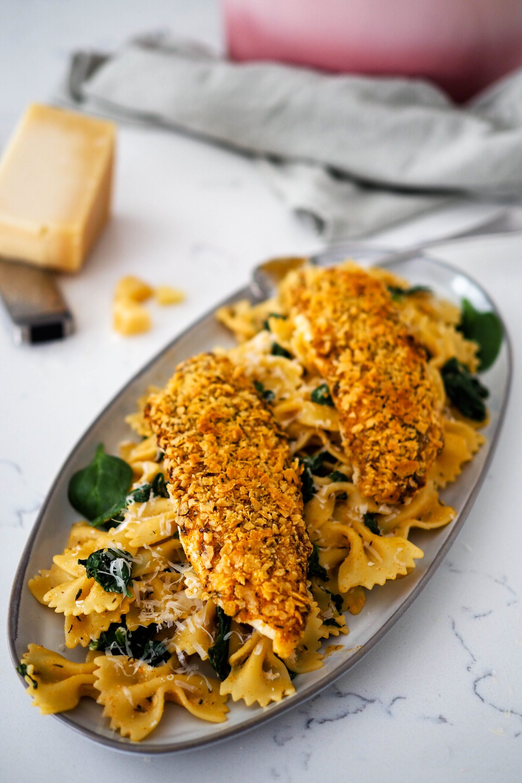 Two breaded tilapia filets on top of a pile of Cajun pasta and spinach.
