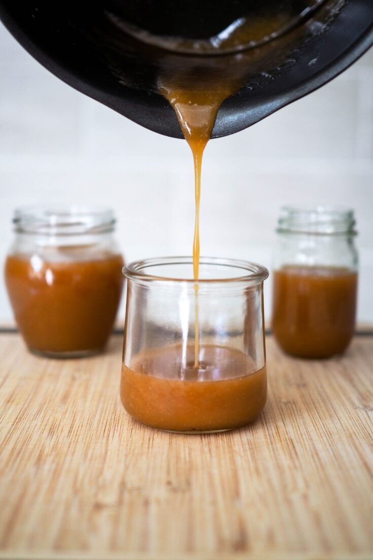 A pot pours salted caramel sauce into a small jar.