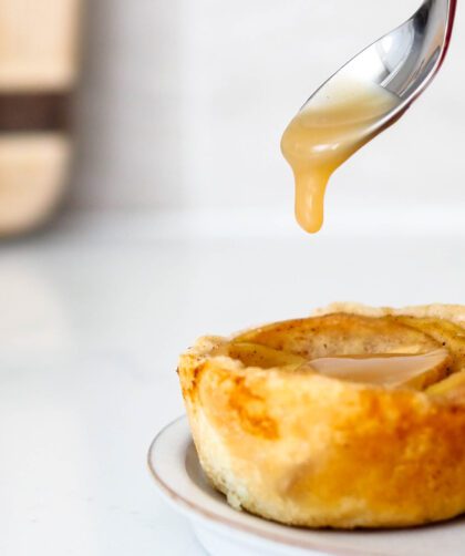 A spoon drops salted caramel onto a mini caramel apple pie.