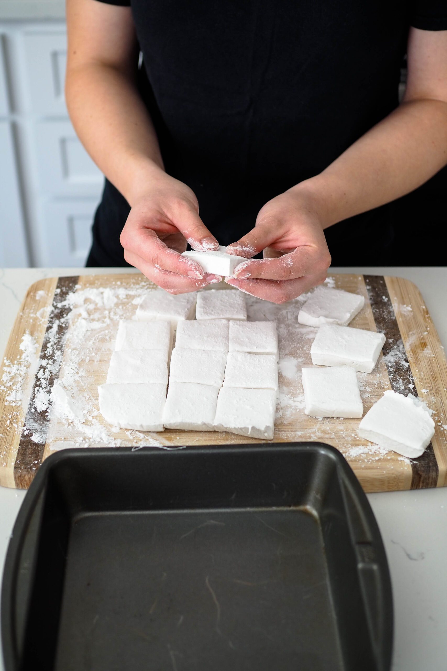 Two hands dust each side of the freshly cut marshmallow with powdered sugar.