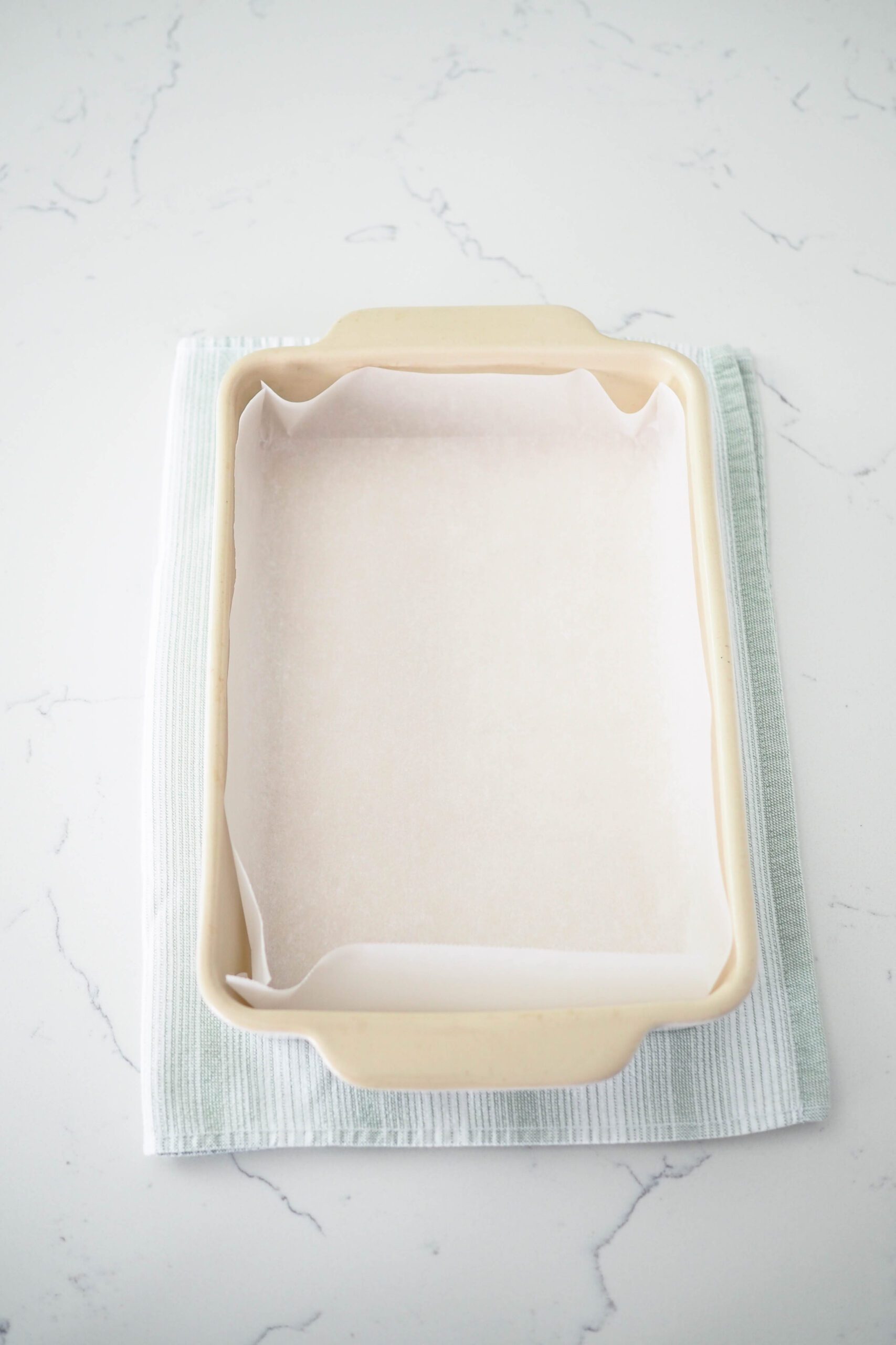 A stoneware baking dish is lined with parchment paper.
